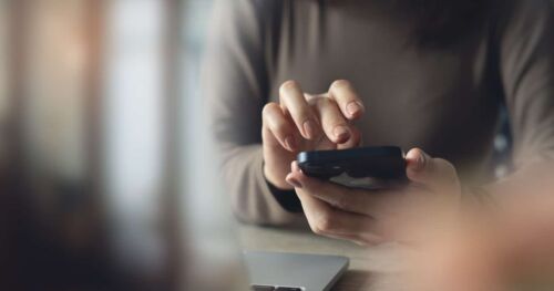 Close up, business woman using mobile phone with laptop computer on office table. Woman using smartphone for online shopping and digital banking via mobile app, social media marketing