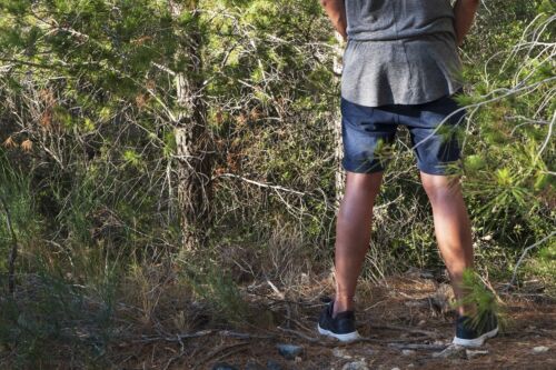 young man peeing in the woods