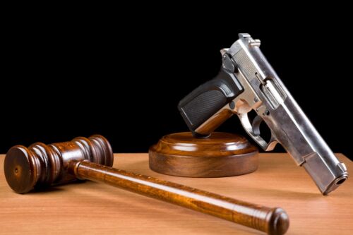 Wooden Gavel And Handgun On Table For Crime Punishment Concept.The background is black.The gun is placed on the right of frame while gavel is seen on the right side.The desk is brown wood.The photo was shot with a full frame DSLR camera in horizontal composition and in studio.Nobody is seen in photo.